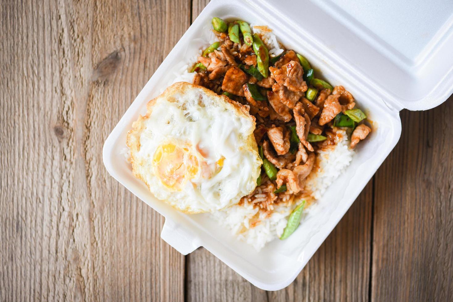 Stir fried pork with red curry paste and basil leaves with yardlong bean and fried egg topped in a plastic box, Thai street food or food delivery photo