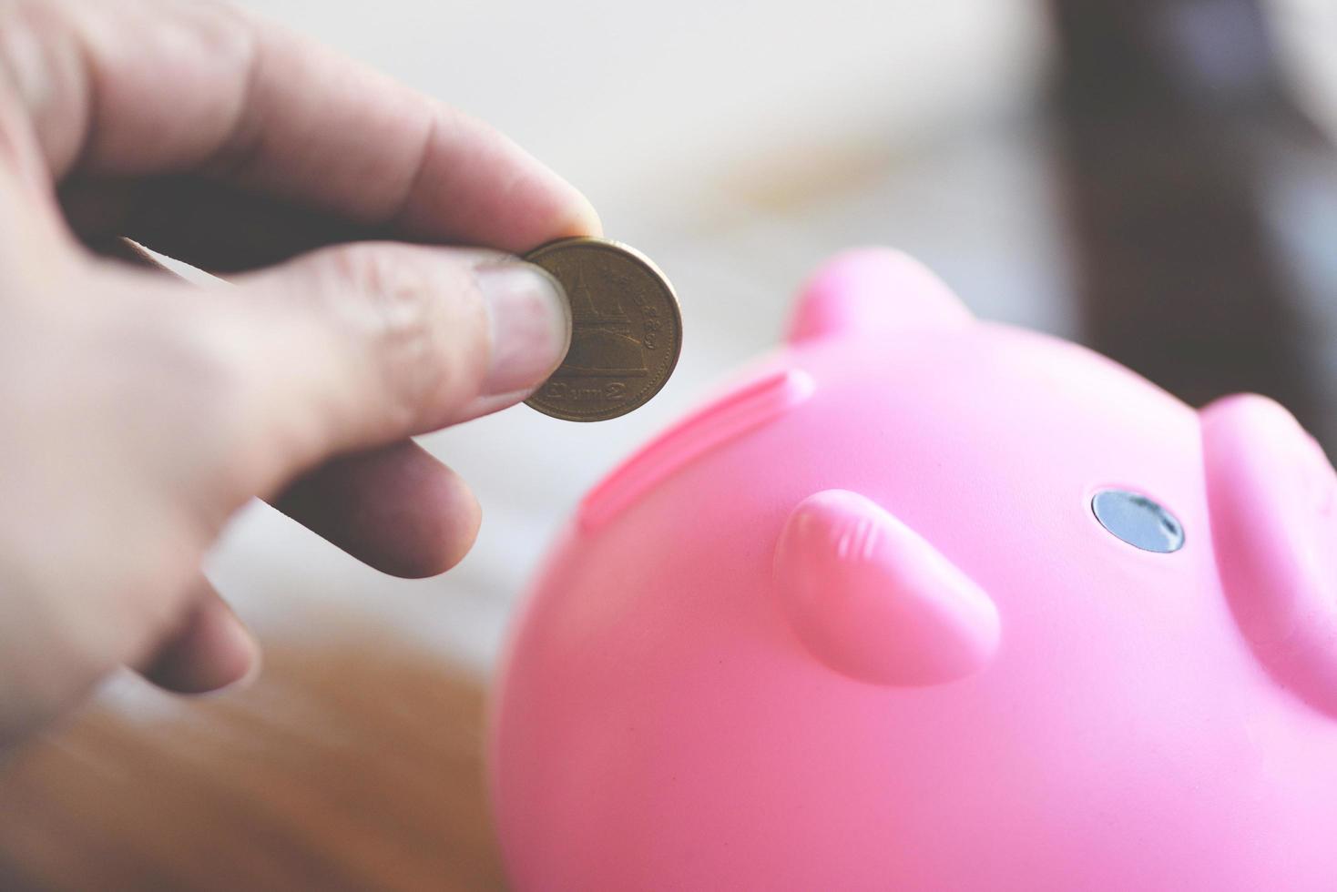 hand man putting money coin into piggy bank at table at home close up - save money for scholarships concept photo