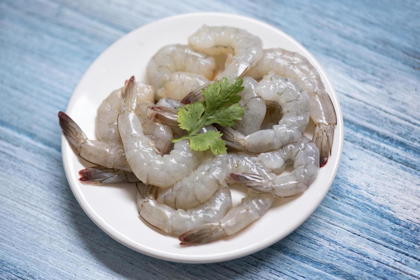 Camarones frescos o gambas, mariscos en estantería - camarones crudos en un plato blanco y fondo de madera para cocinar foto