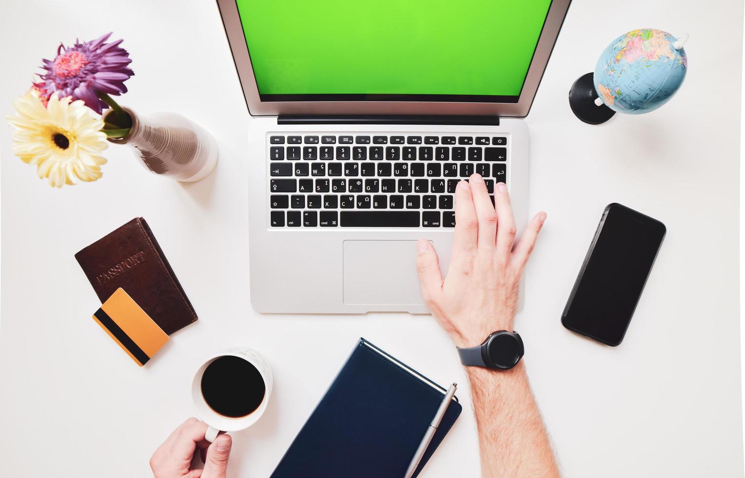 Creative flat lay of workspace desk with laptop, passport, camera, smartphone, bank card, coffee in hand on white color background. Travel lifestyle concept green screen space desktop. photo