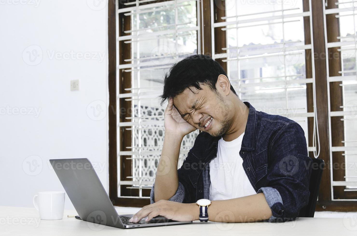 Young Asian man feeling stress and confuse when work laptop on table. photo