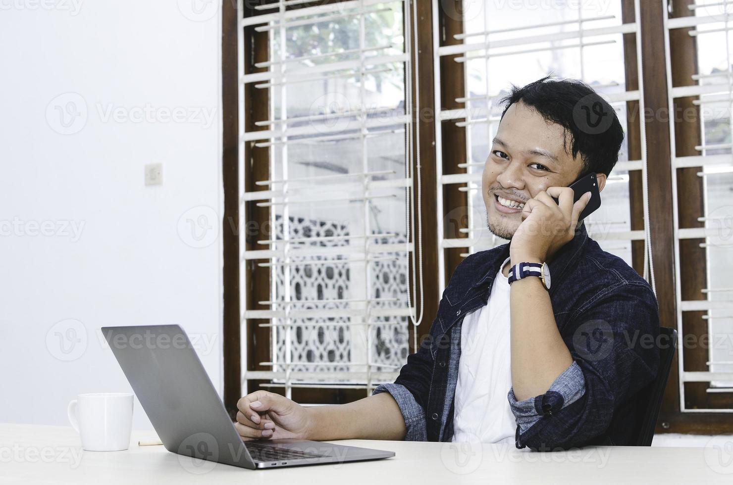 Young Asian man happy and smile what he see in the laptop when in call on smartphone photo