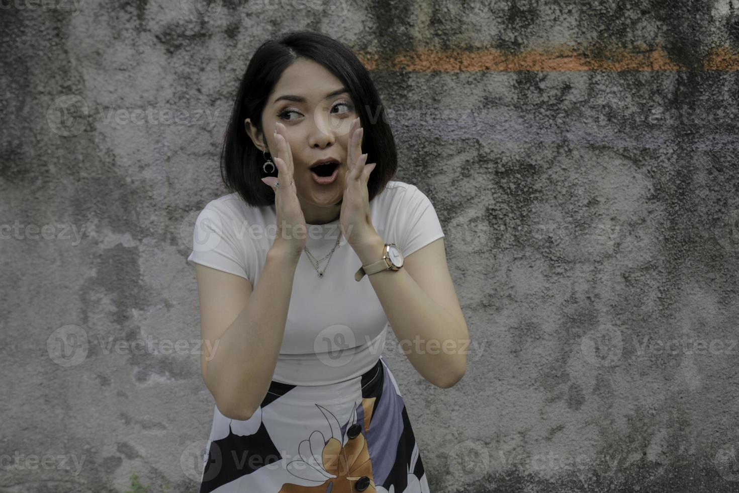 Young Asian Woman is shouting with mouth wide open and isolated grey wall photo