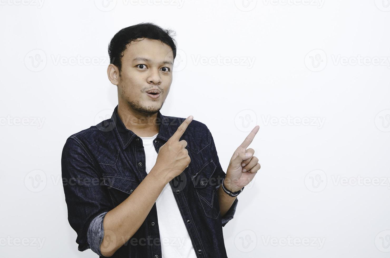 Wow and shock face of young Asian man in white shirt with hand point on above empty space. photo