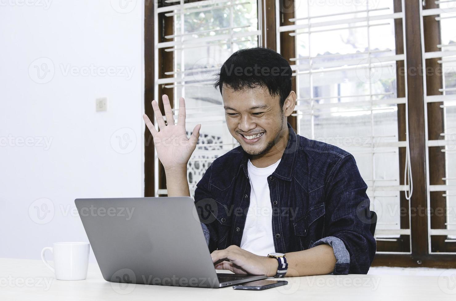 Young Asian man happy and excited when video call with laptop on table. photo