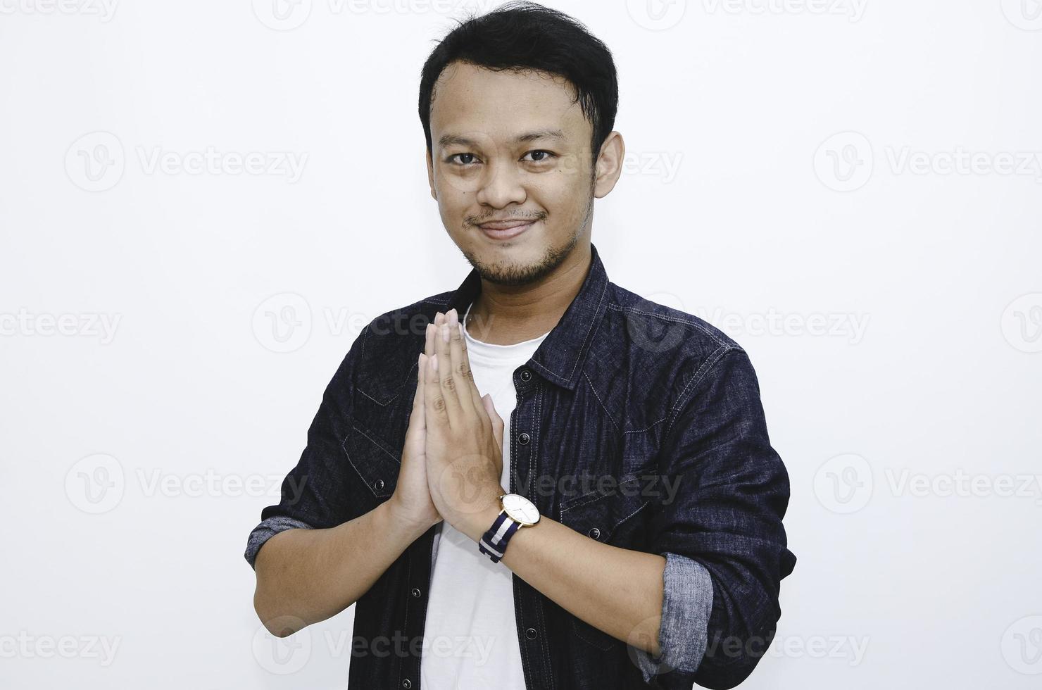 joven asiático vistiendo manos de saludo. hombre indonesio sobre fondo gris. foto