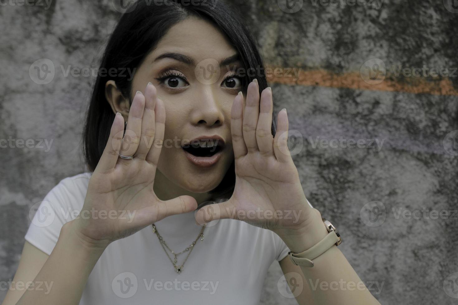 una joven asiática grita con la boca abierta y una pared gris aislada foto
