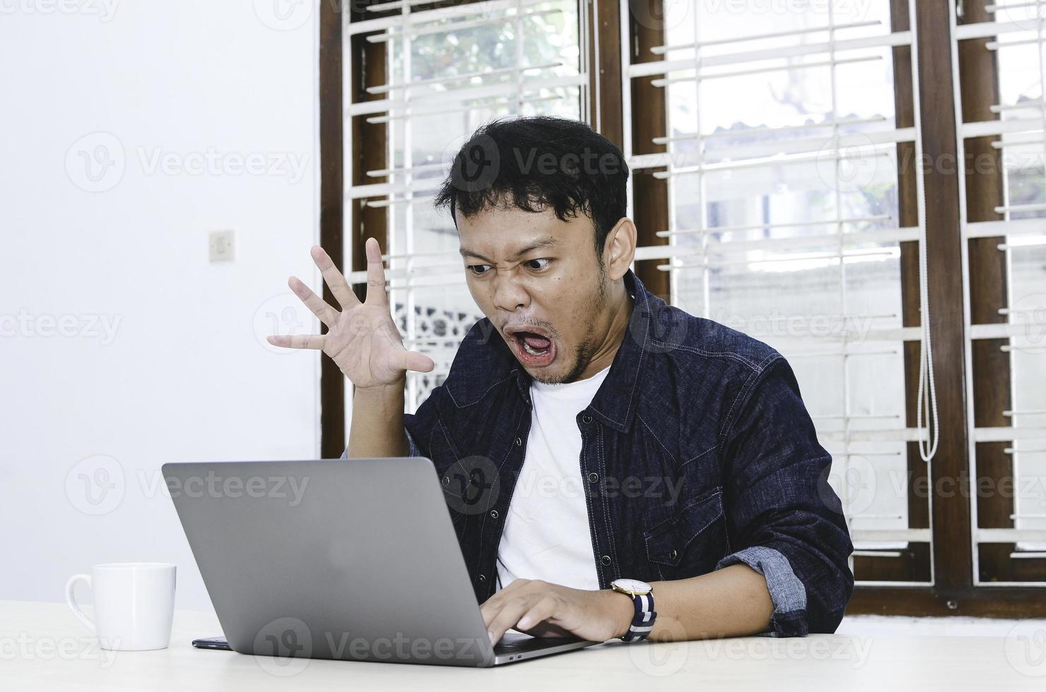 joven asiático sorprendido y asombrado por lo que ve en la computadora portátil. foto
