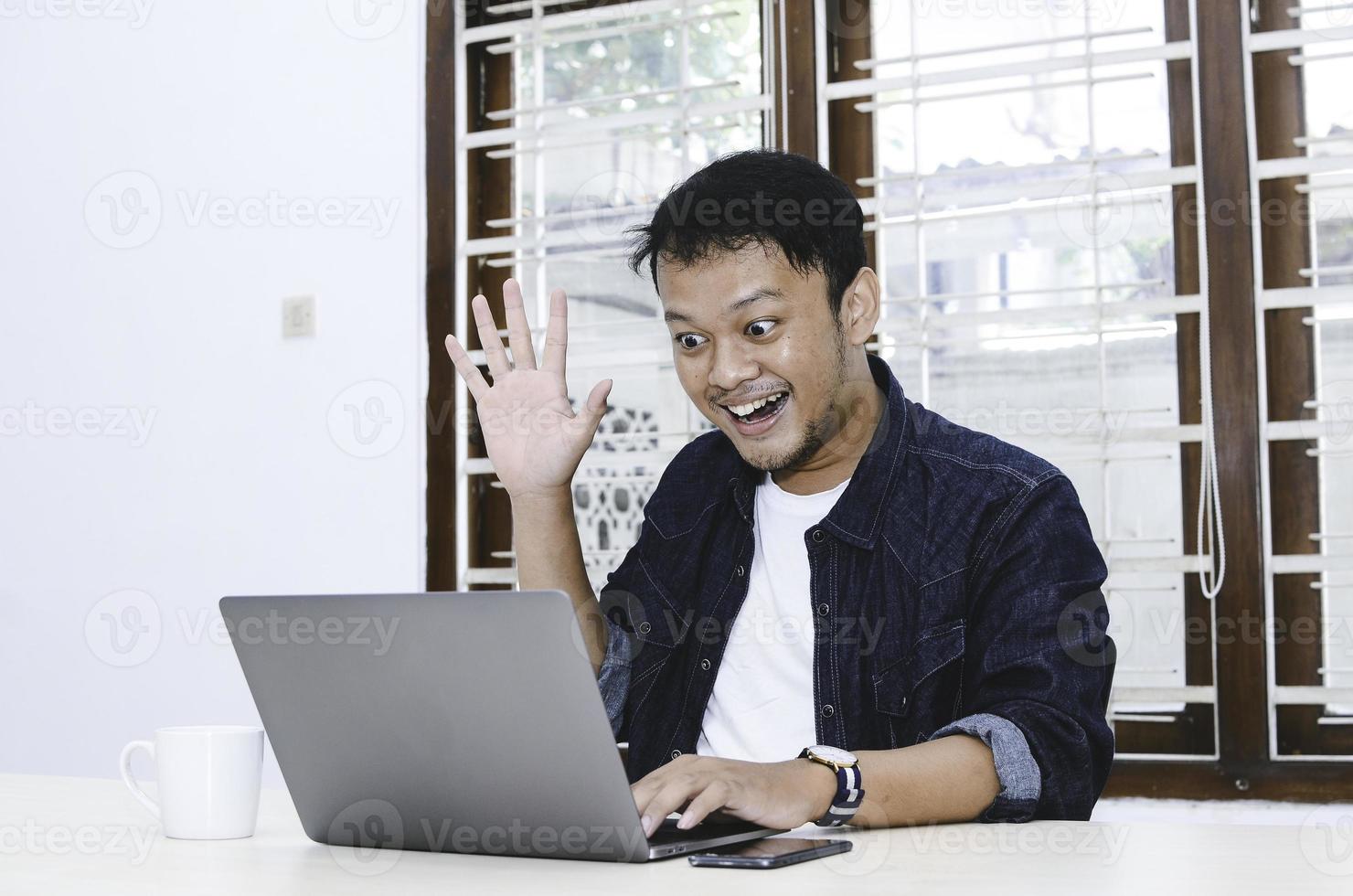 Young Asian man happy and excited when video call with laptop on table. photo