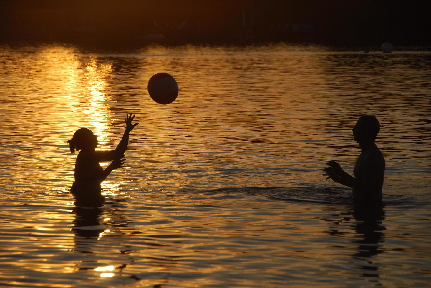 pareja jugando a la pelota en el mar durante la puesta de sol foto