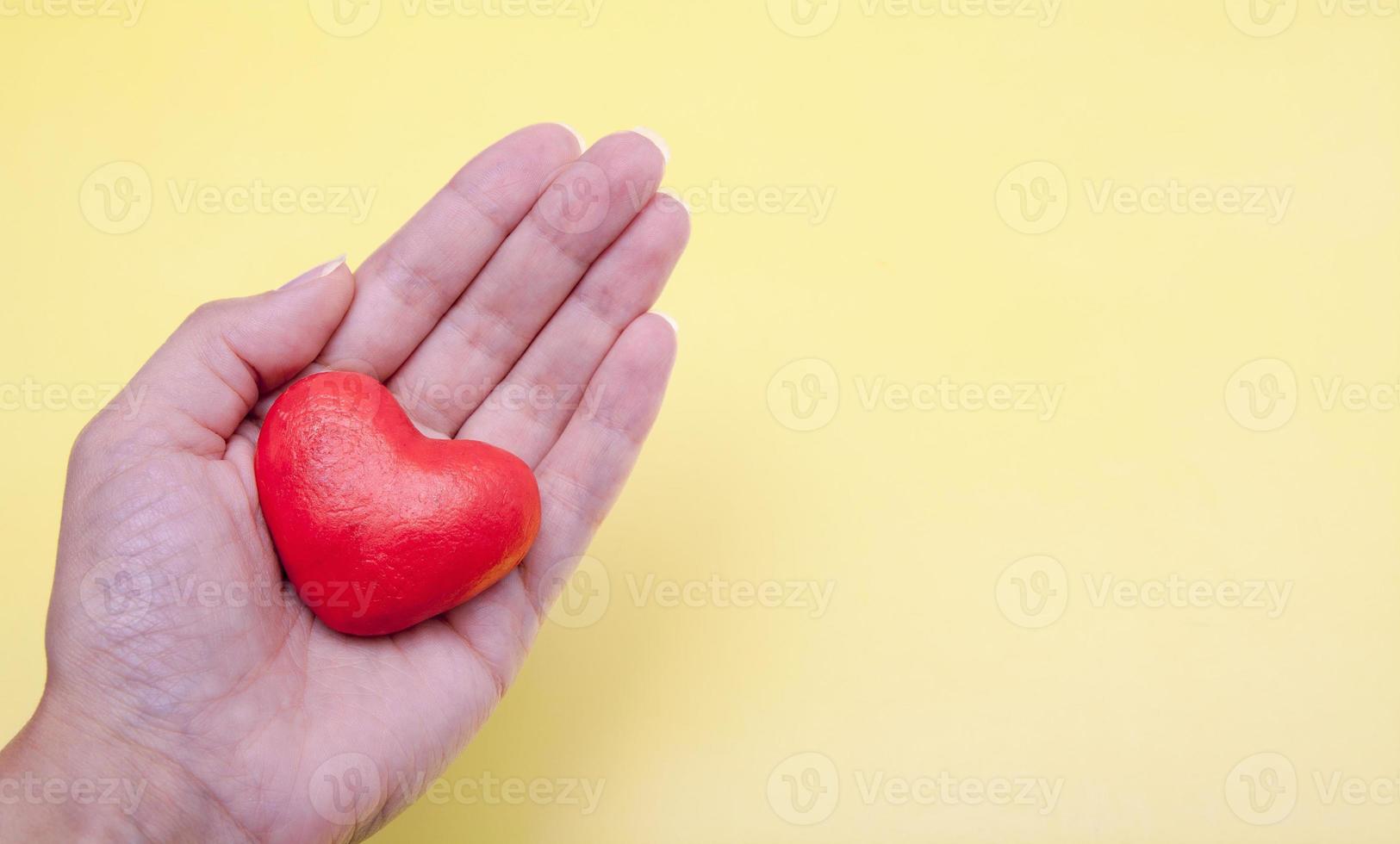 corazón rojo en la mano sobre un fondo amarillo con espacio de copia. día internacional de la caridad, concepto de donación foto