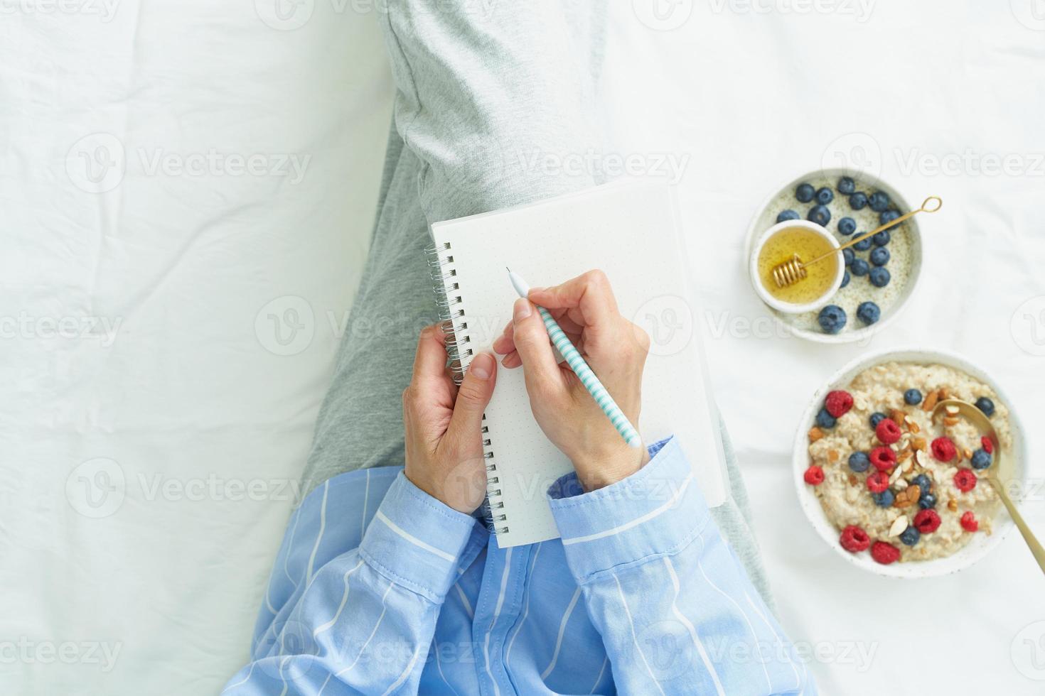 woman writes in large white open notebook, lay on bed photo