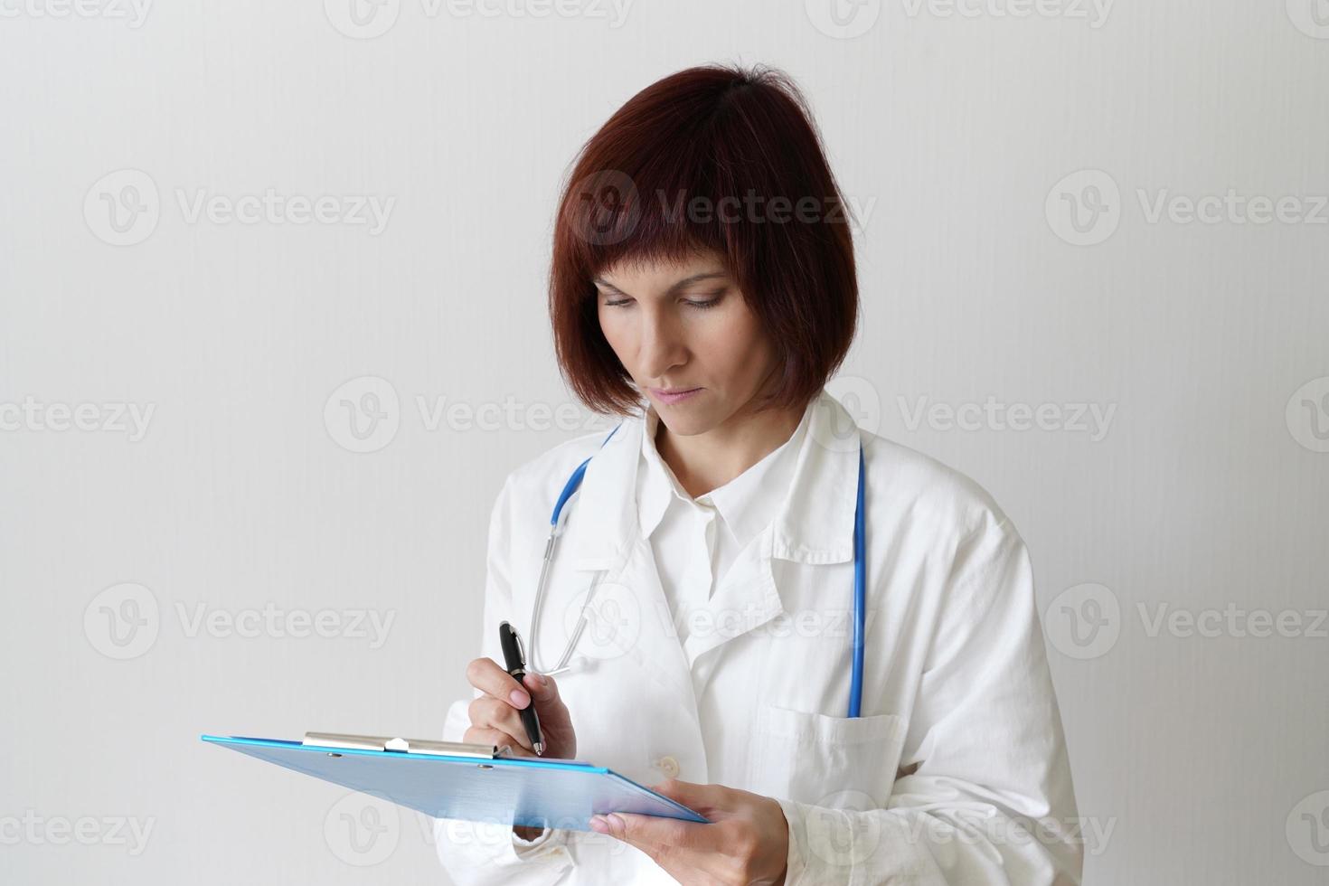 Female adult doctor stands on white background. Beautiful woman, thinking, writing photo