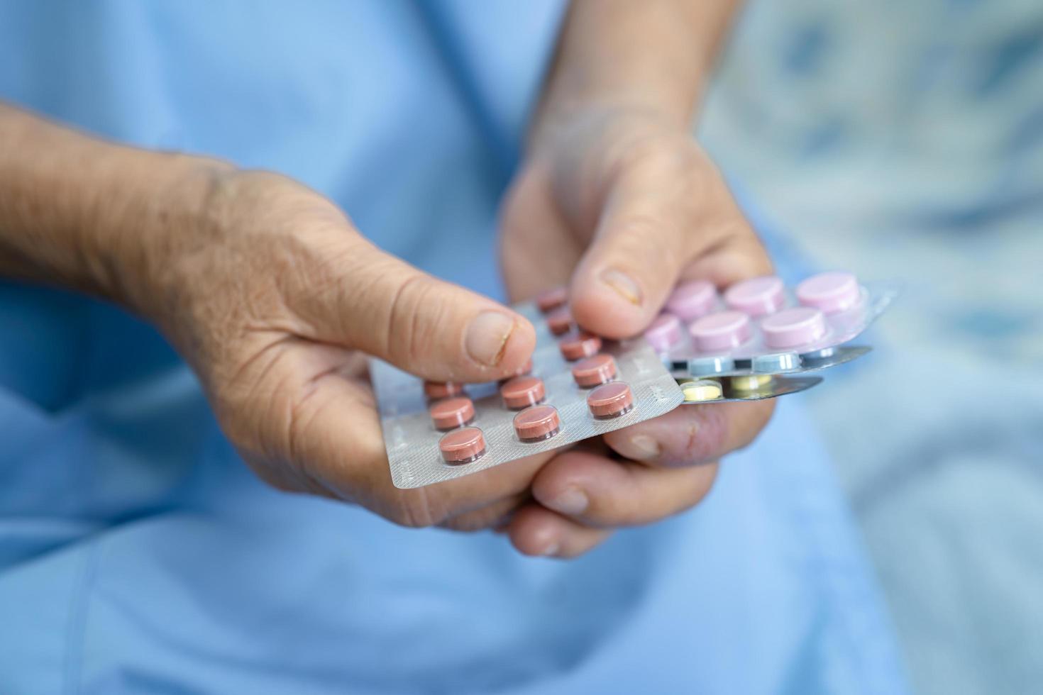 Asian senior or elderly old lady woman patient holding antibiotics capsule pills in blister packaging for treatment infection patient in hospital, Pharmacy drugstore concept. photo