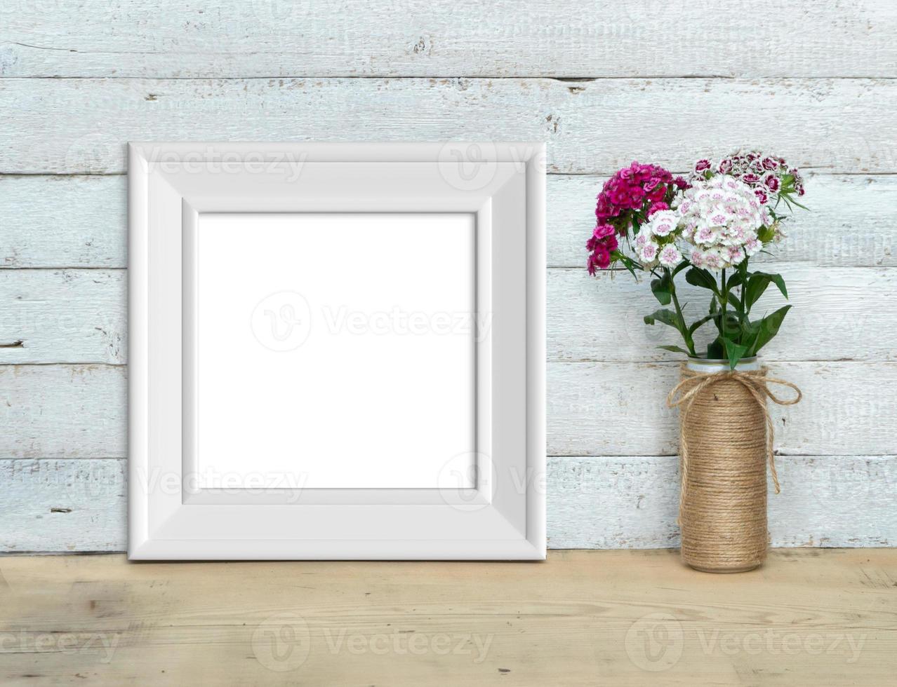 Square Vintage White Wooden Frame mockup near a bouquet of sweet-william  stands on a wooden table on a painted white wooden background. Rustic style, simple beauty. 3d render. photo