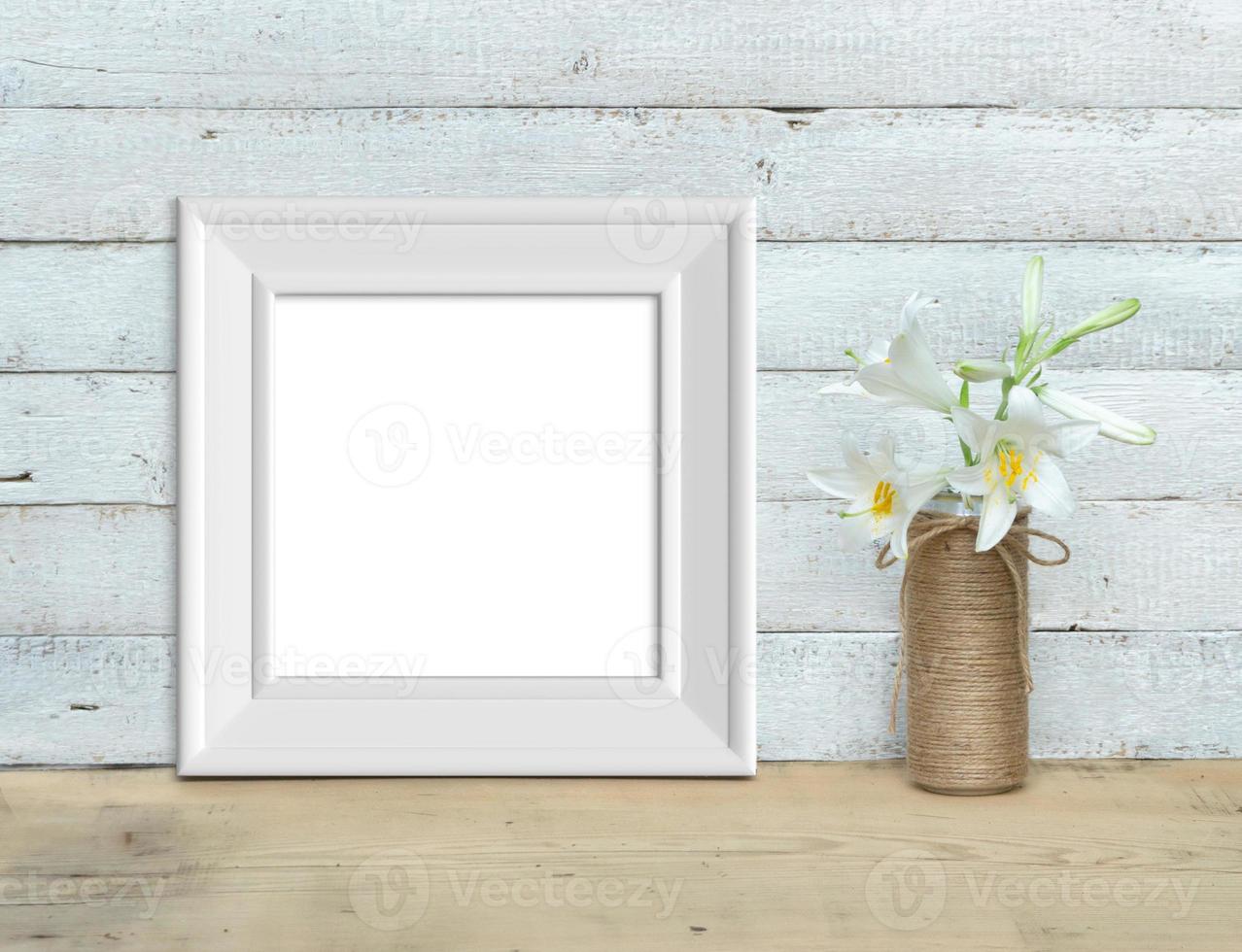 Square Vintage White Wooden Frame mockup near a bouquet of lilies stands on a wooden table on a painted white wooden background. Rustic style, simple beauty. 3d render. photo