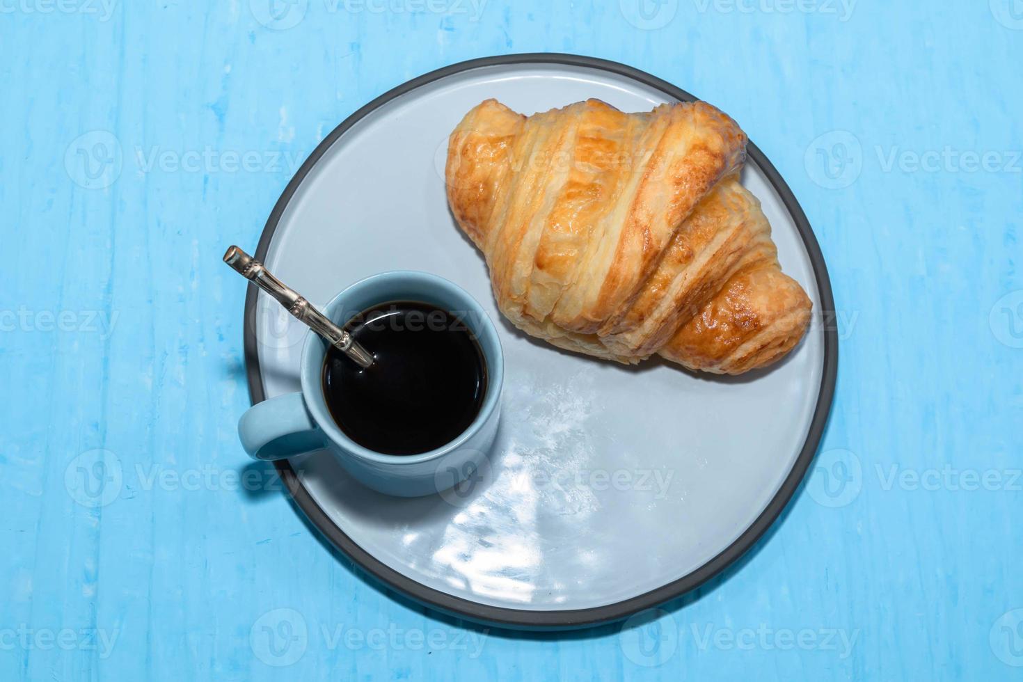 desayuno comida croissant en plato y café en mesa azul. foto