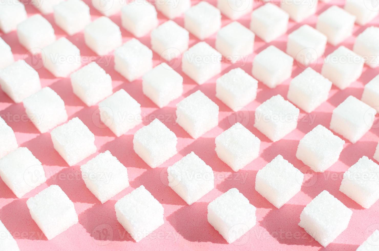 azúcar refinada sobre fondo rosa. cubos de azúcar dulce y blanco en forma geométrica. sombras duras. foto