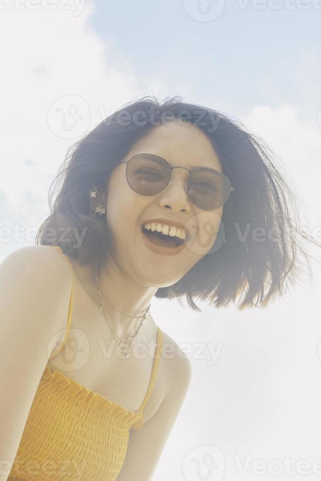 retrato de una mujer asiática feliz y sonriente con vistas al cielo azul desde abajo. foto