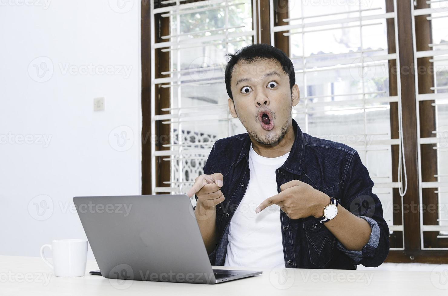 Young Asian man shocked and wow what he see in the laptop. photo