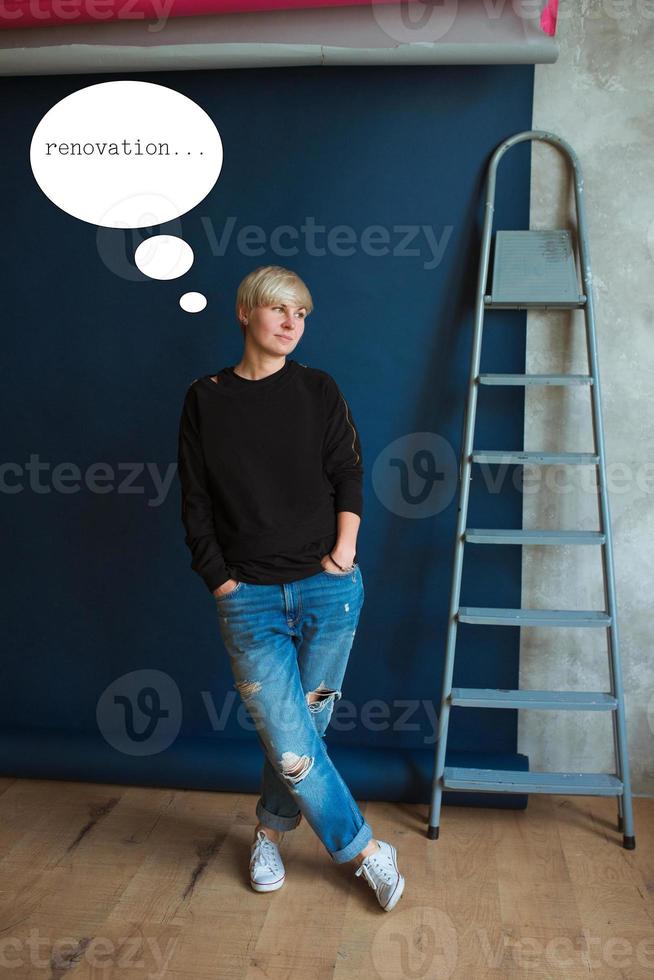 joven rubia moderna con sudadera negra y jeans parada cerca de la escalera y planeando la renovación foto