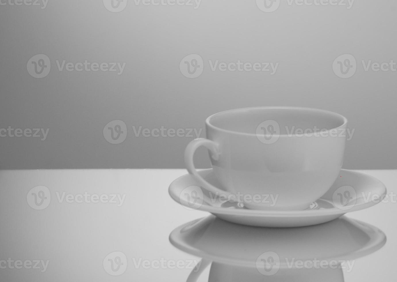 una taza y plato blancos sobre un fondo claro con reflejo foto