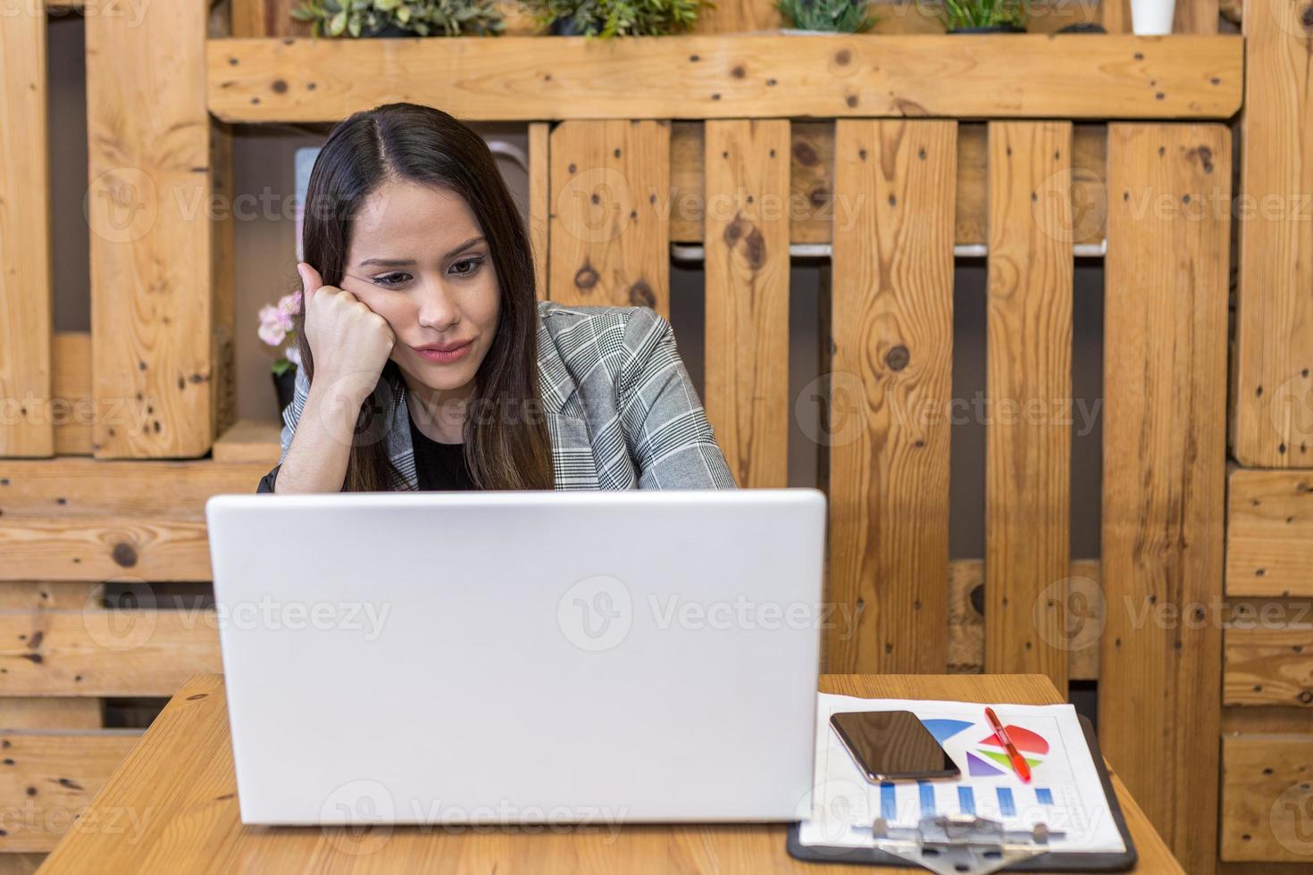 mujer aburrida apoyada en la mano mientras usa la computadora portátil foto