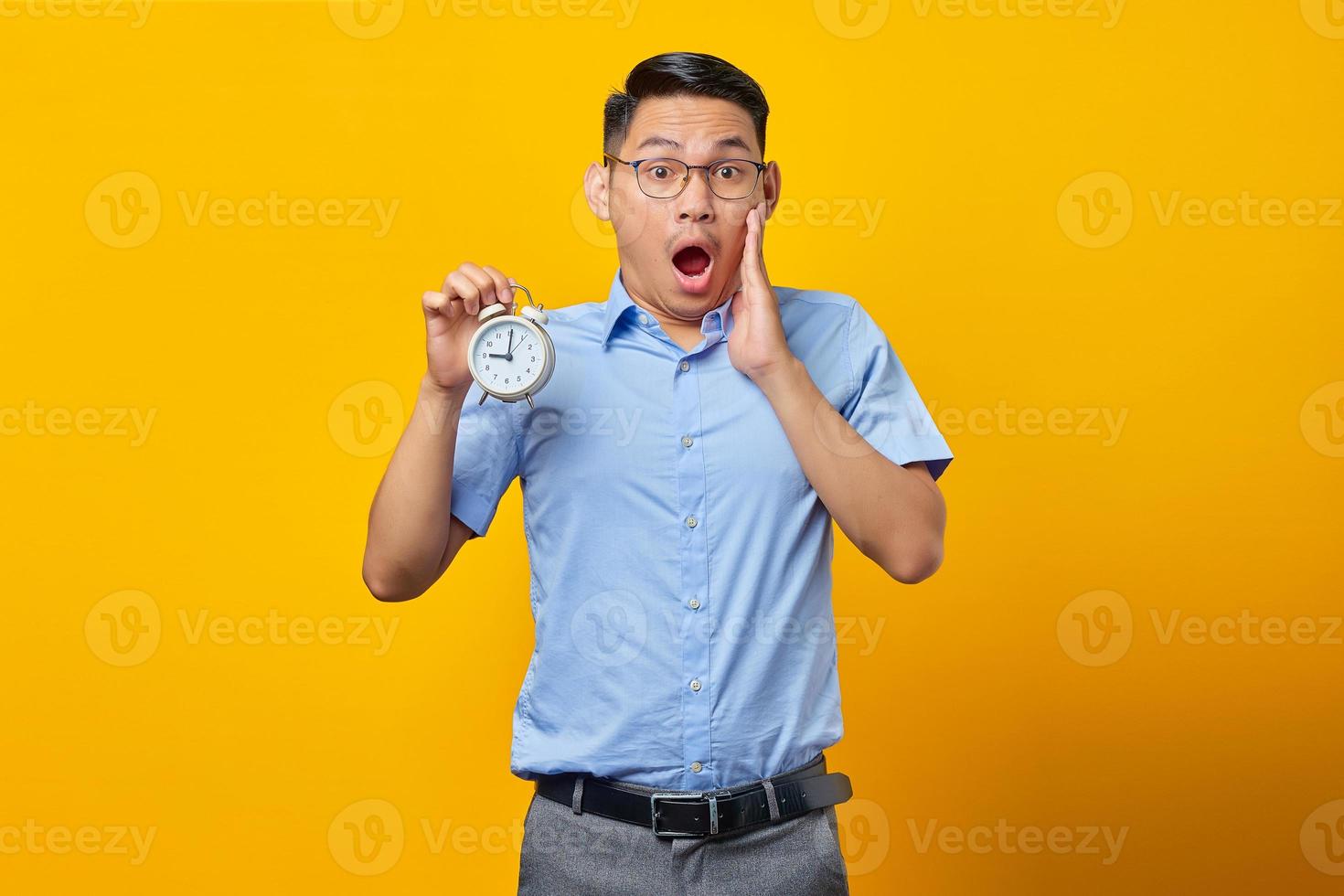 Shocked young Asian woman in glasses holding document folder with open mouth isolated on yellow background. Time management lifestyle concept photo