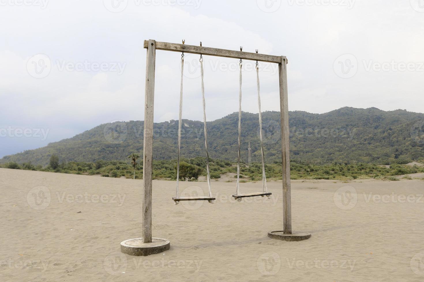 The old rope wooden swing on the desert or sandy beach with mountain background photo