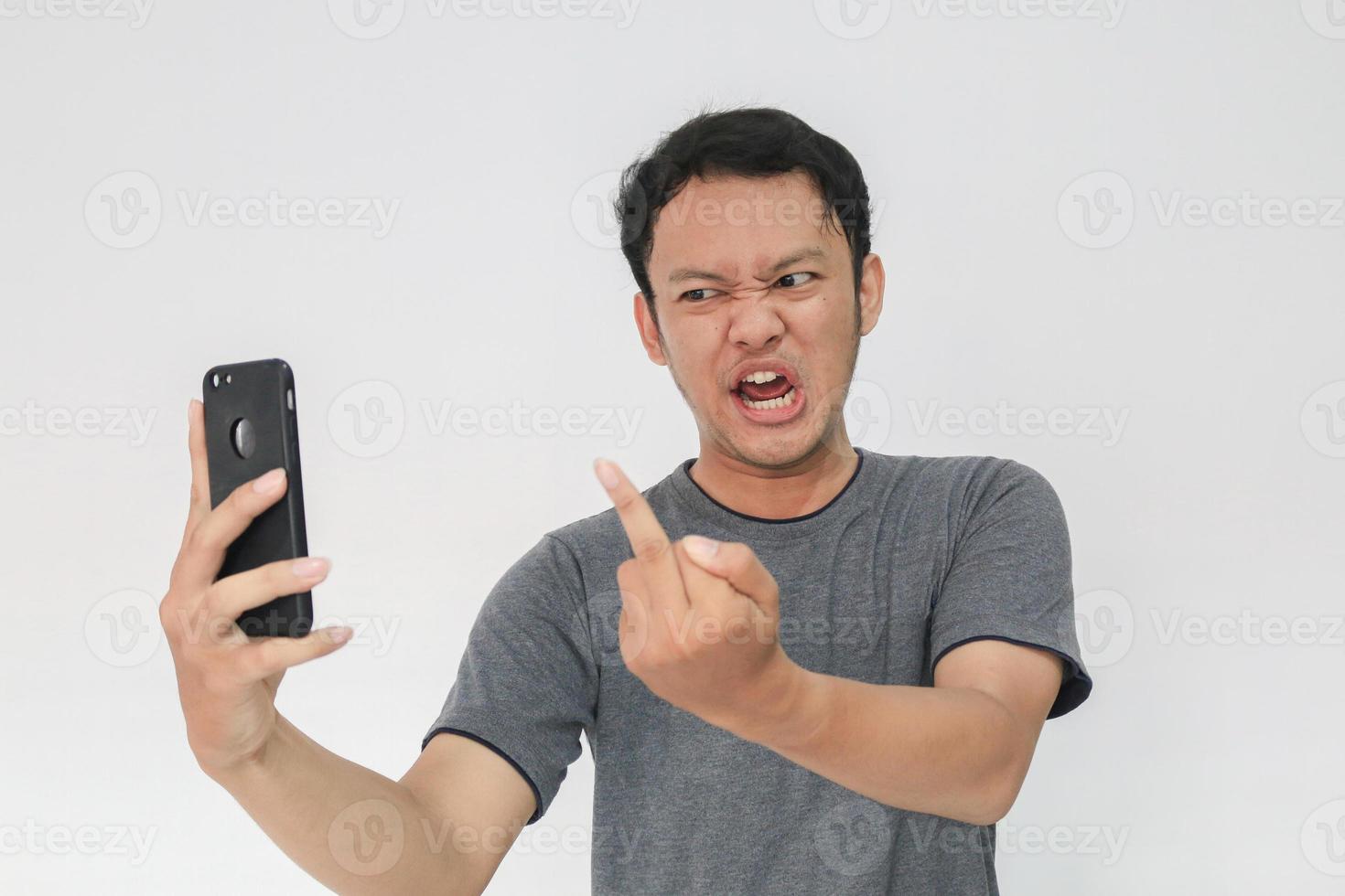 un joven asiático enojado se enoja con el teléfono inteligente. indonesia el hombre usa camisa negra aislado fondo gris. foto