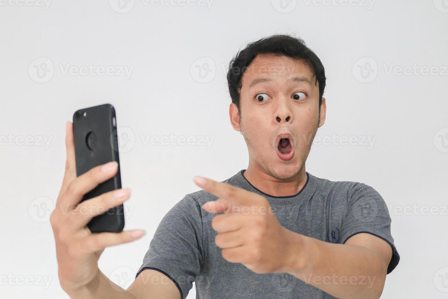 Wow face of Your Asian man shocked what he see in the smartphone on isolated grey background. photo