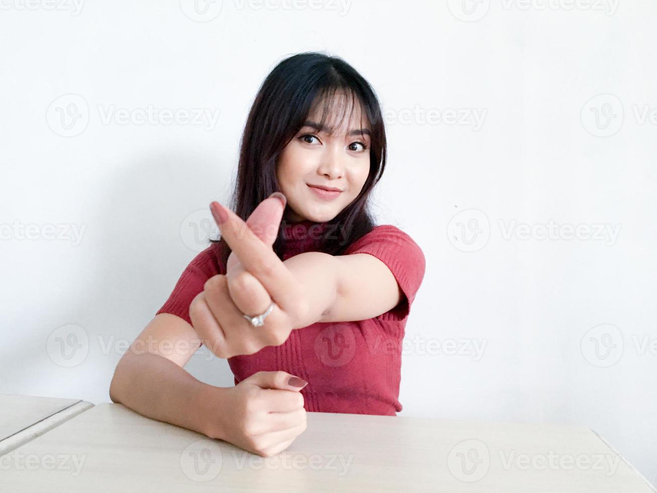 hermosa chica asiática sonriente mostrando el amor signo de corea con el dedo con fondo borroso fondo blanco aislado. mujeres indonesias foto
