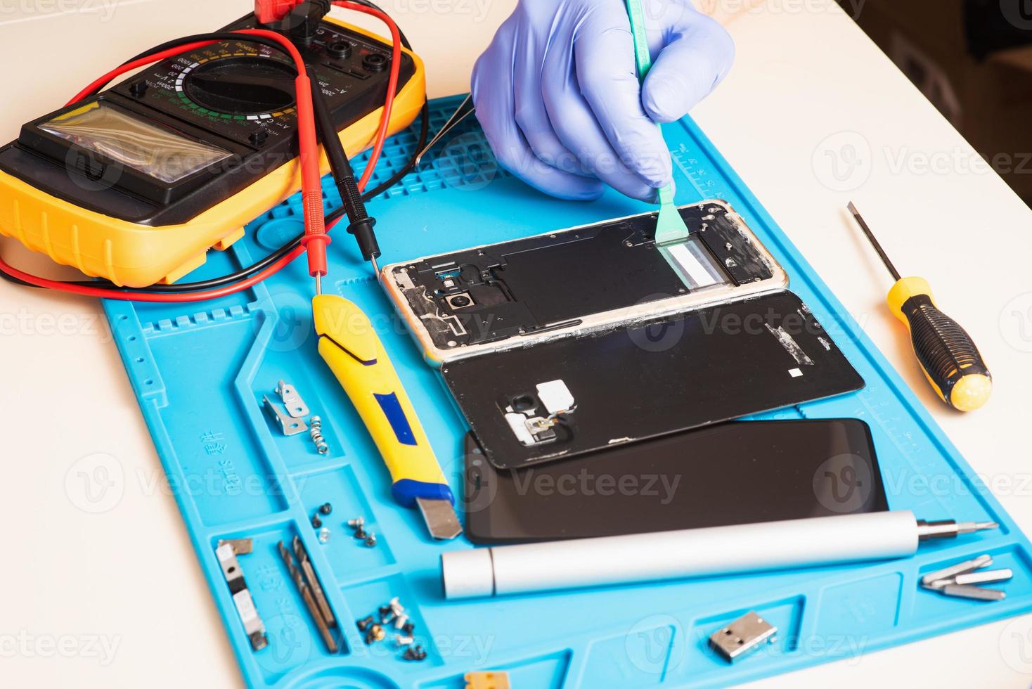 el artesano en guantes de goma repara o repara un teléfono móvil en una alfombrilla de goma especial para reparar. vista desde el interior foto