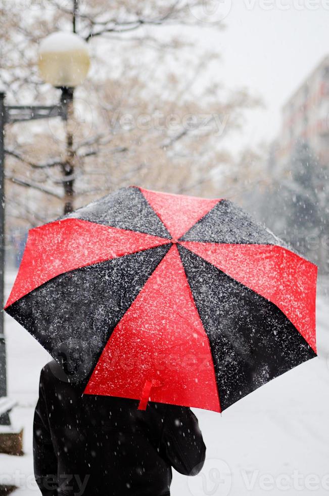 mujer sosteniendo un paraguas negro y rojo bajo la nieve foto