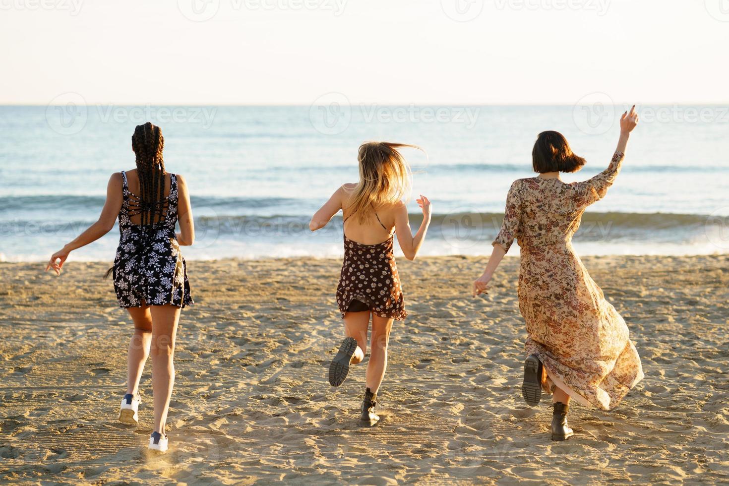 novias en vestidos de verano corriendo hacia el mar agitado foto