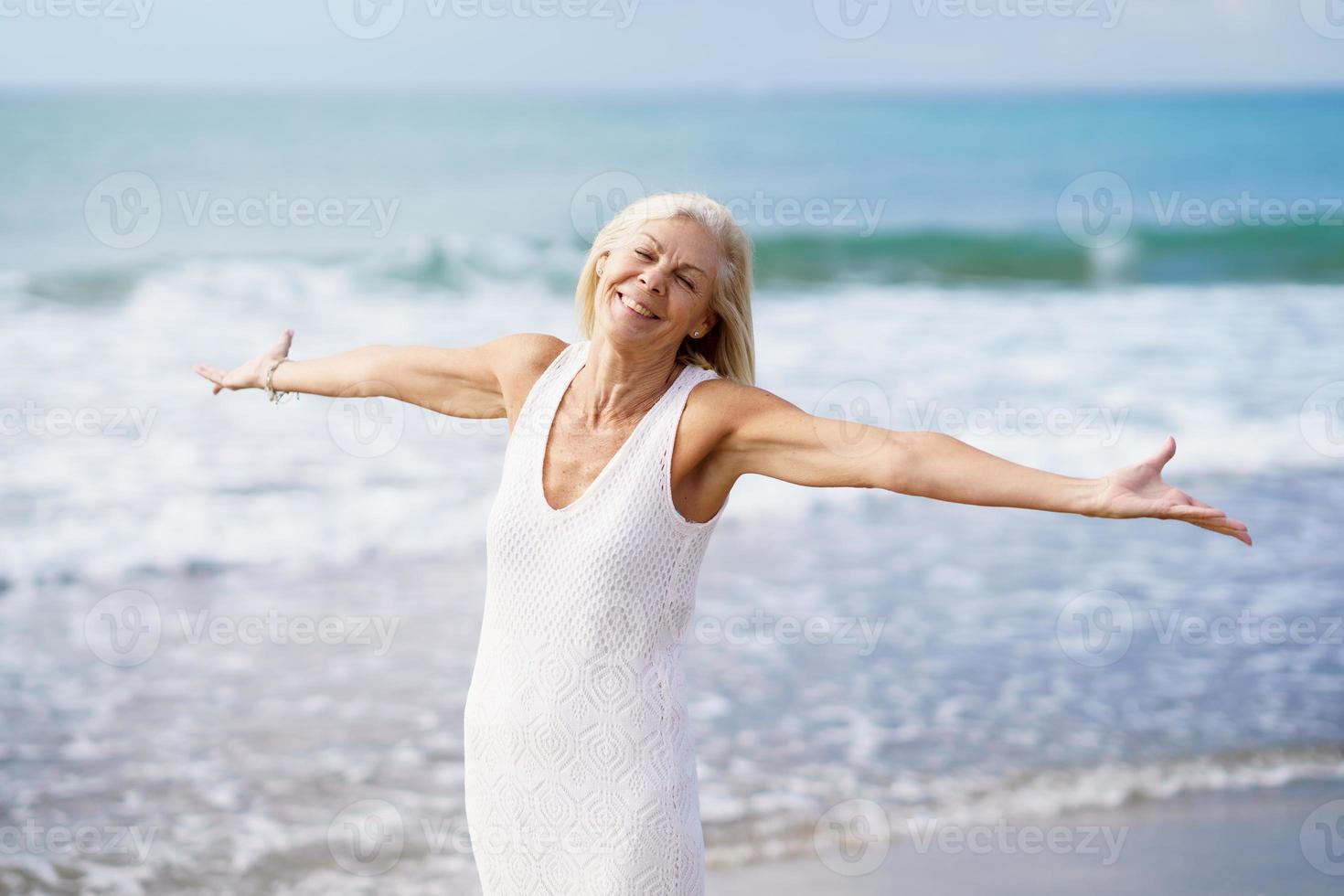 Happy mature woman opening her arms on the beach, spending her leisure time, enjoying her free time photo