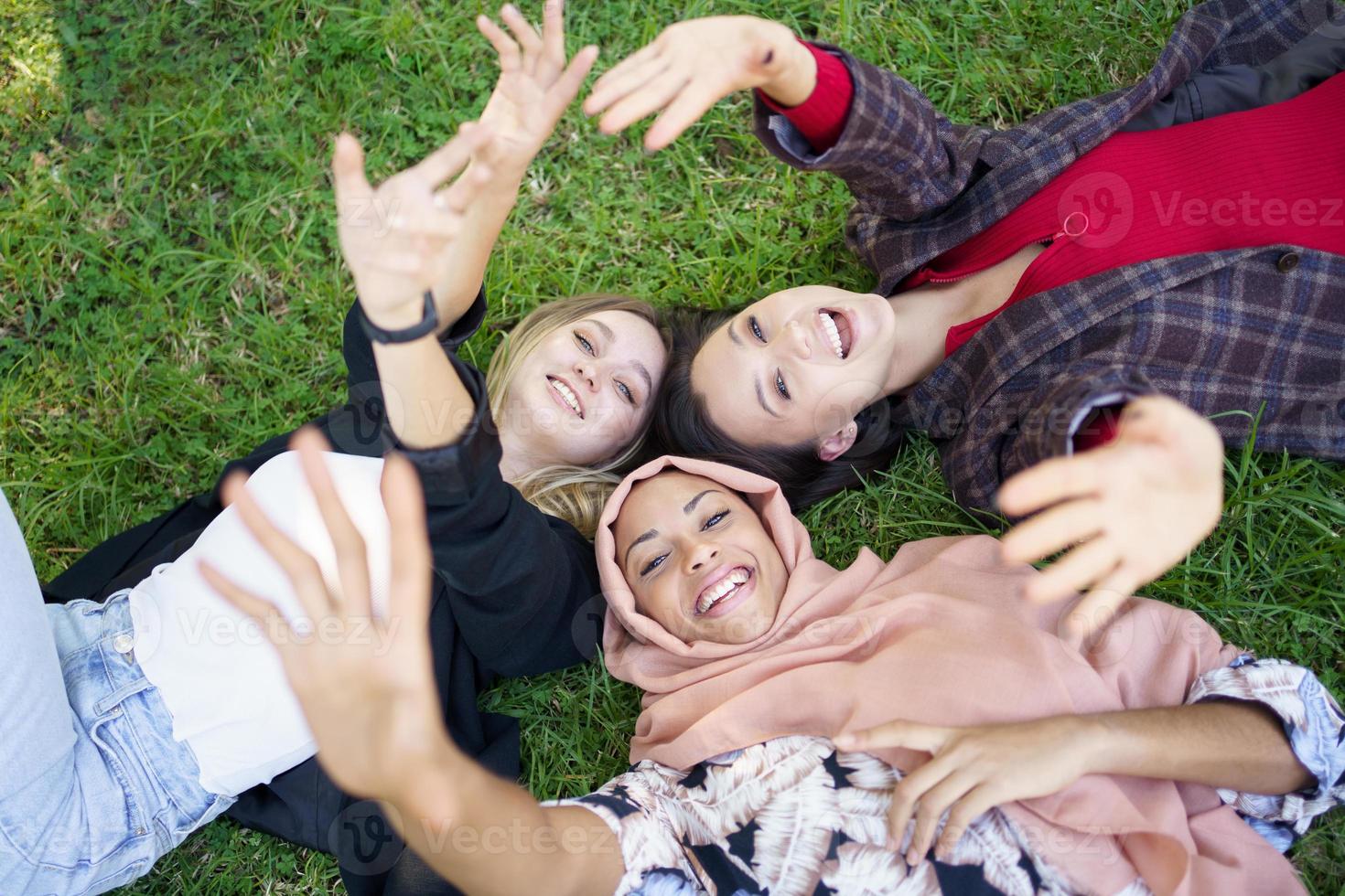 Cheerful young diverse female friends lying on grass and smiling at camera photo