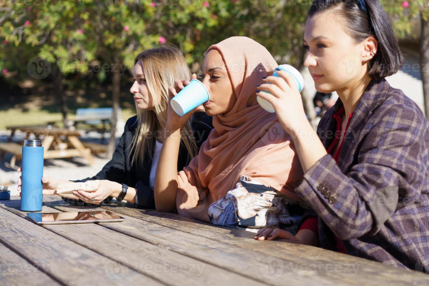 tres chicas diversas tomando café y charlando en el parque de la ciudad foto