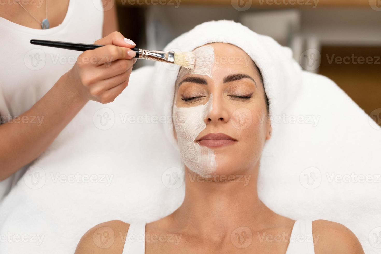 Aesthetics applying a mask to the face of a Middle-aged woman in modern wellness center. photo