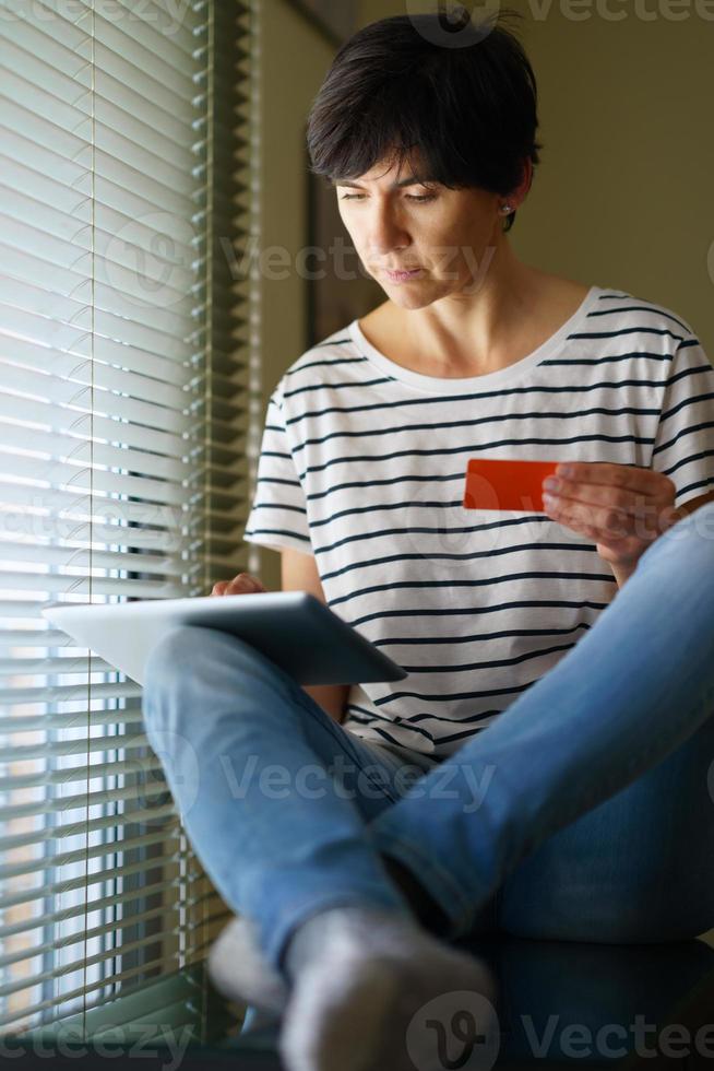 Middle-aged woman shopping online with her digital tablet paying with a credit card. photo