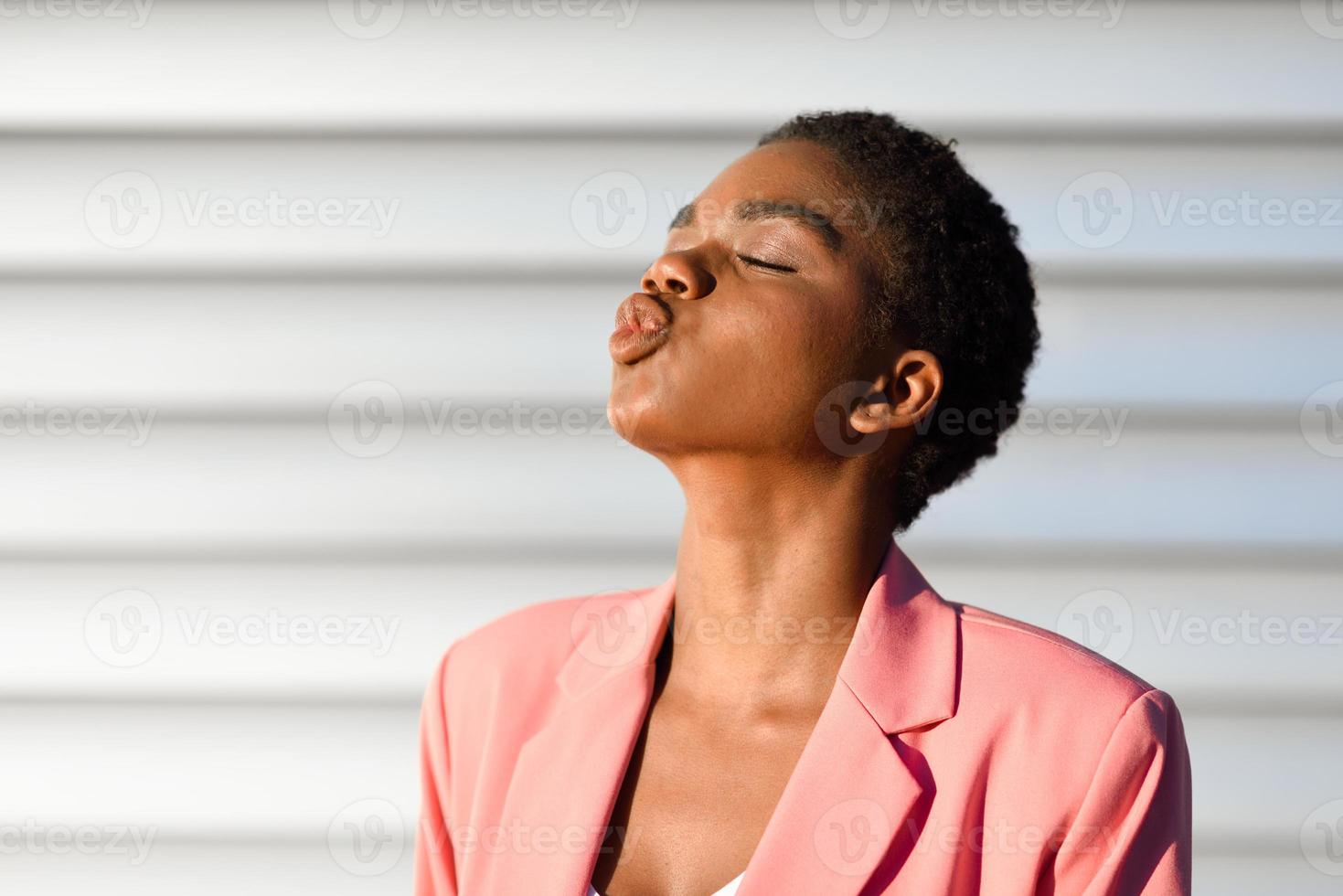 mujer negra, de pelo muy corto lanzando un beso. foto