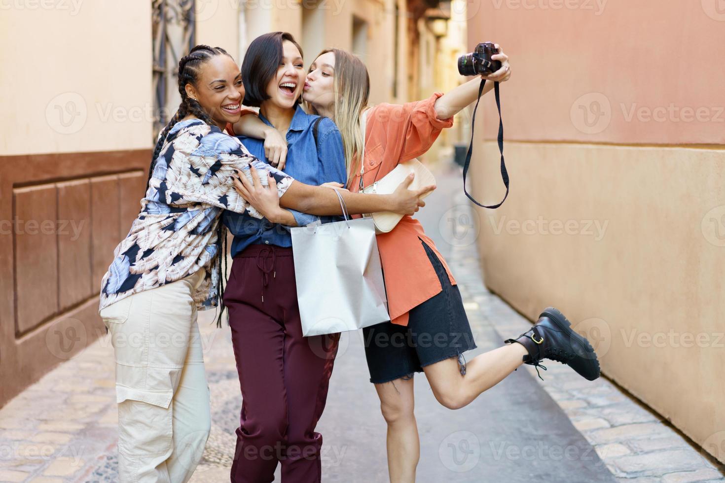 alegres jóvenes diversas mujeres abrazando y tomando selfie en cámara en la ciudad foto