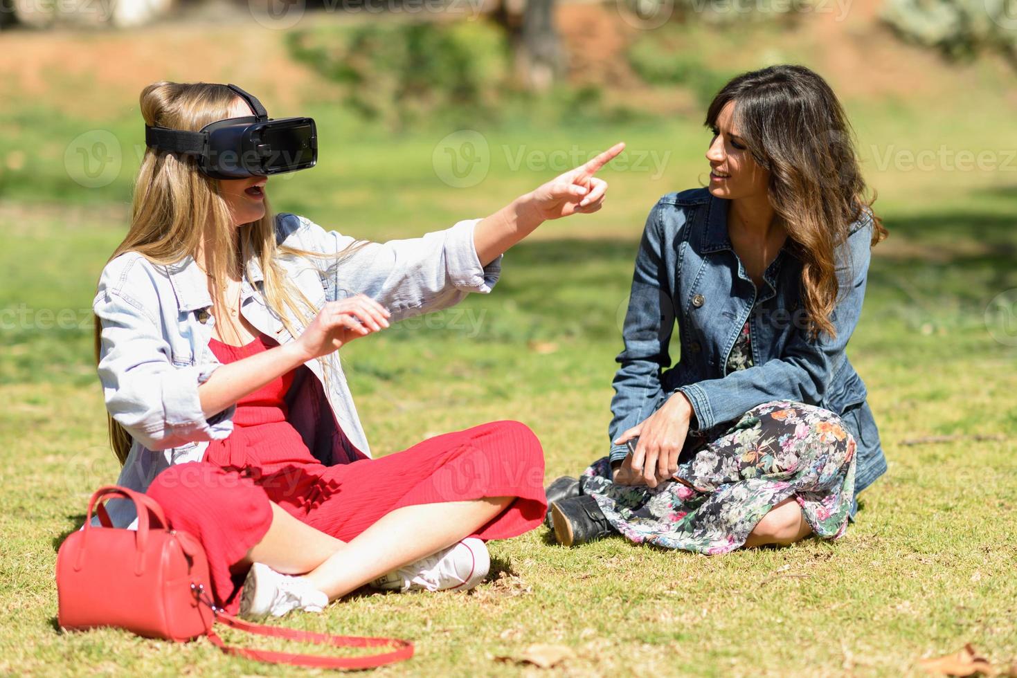 Two women looking in VR glasses and gesturing with his hands outdoor photo