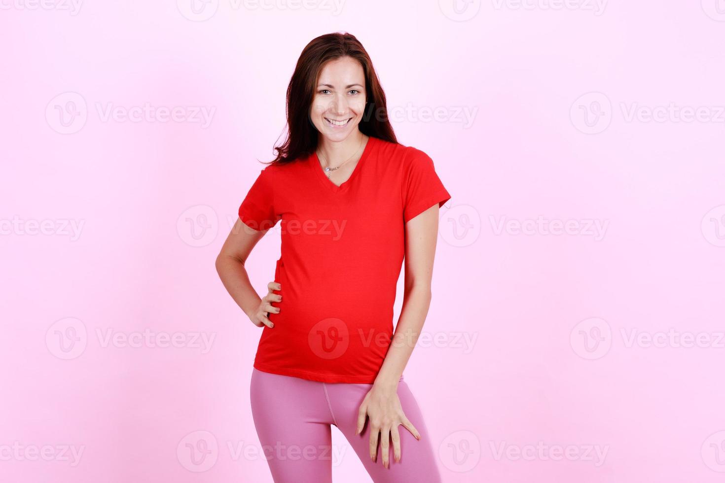 Half length portrait of beautiful caucasian young pregnant model shows her belly with smile face. Pregnant happy new mother posing indoor and looking with proud to camera. Love and family concept photo