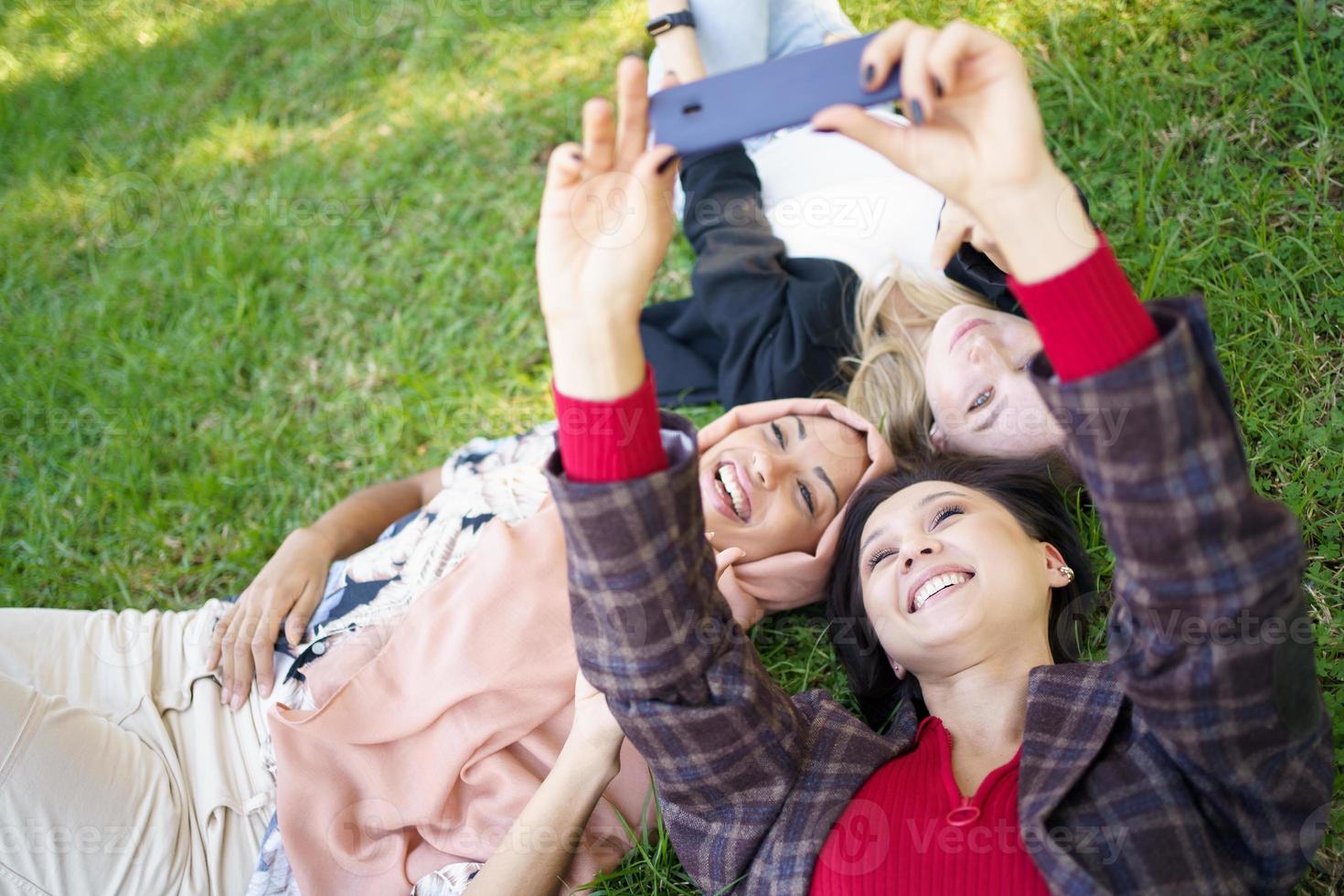 mujeres alegres y diversas tomando selfie en el césped foto