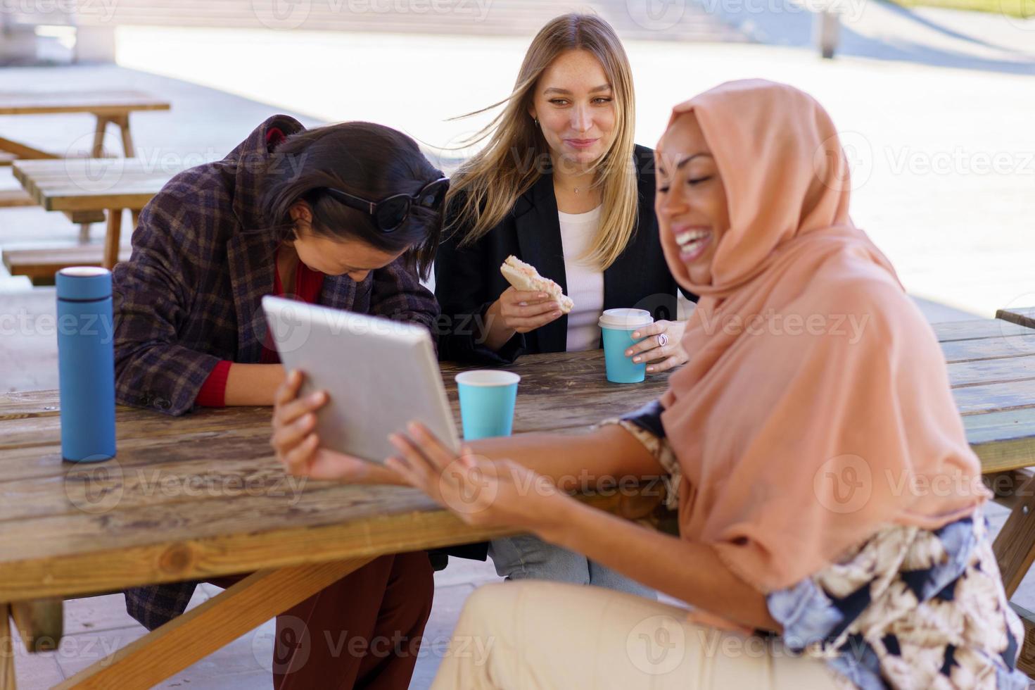 Content young multiracial female friends laughing while sharing tablet in cafe photo