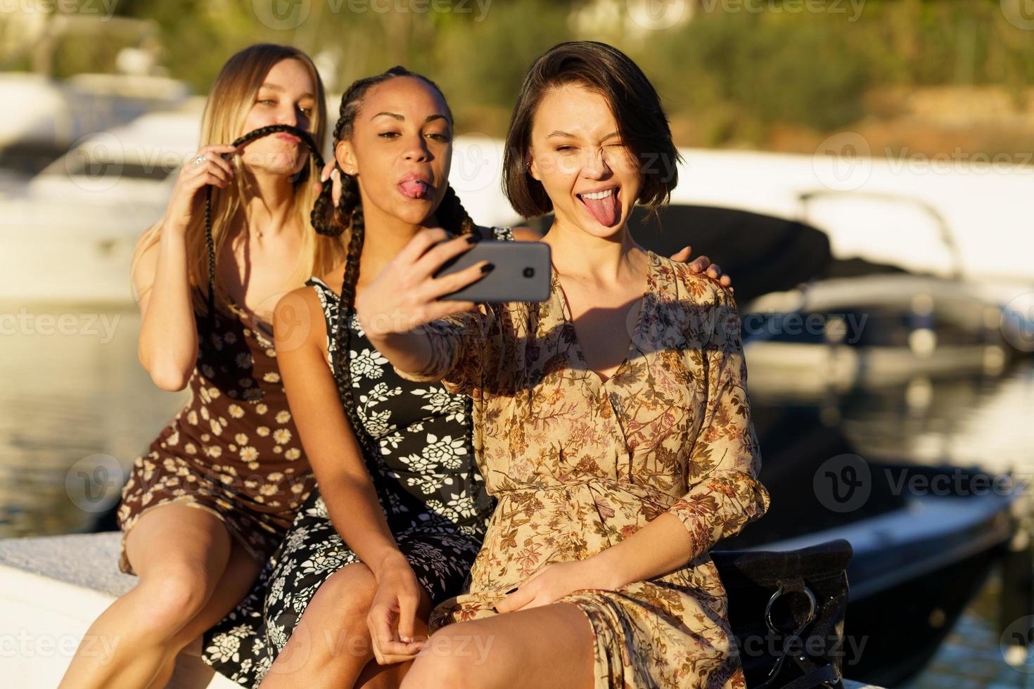Mujeres multirraciales divertidas haciendo muecas mientras toman selfie cerca del río foto
