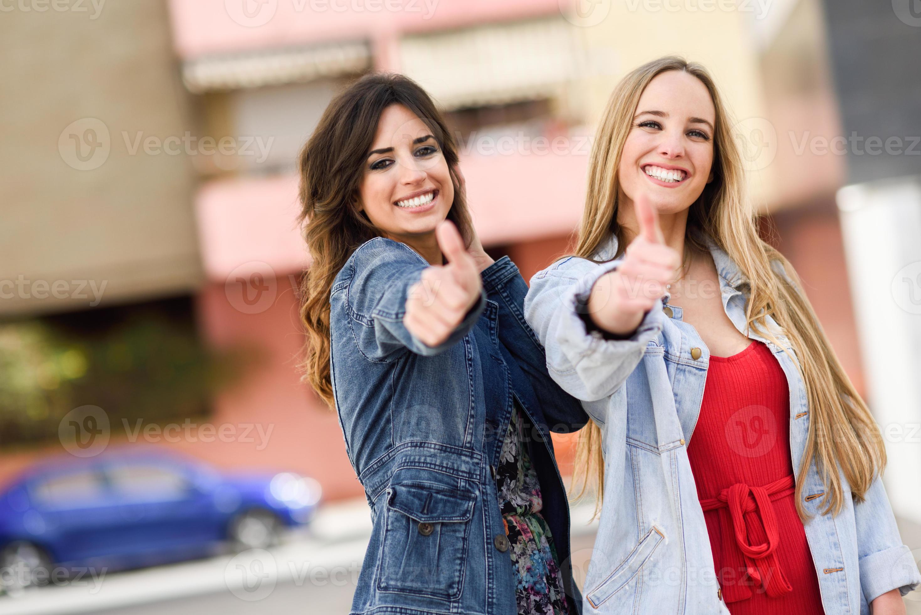 Two young women with thumbs up outdoors