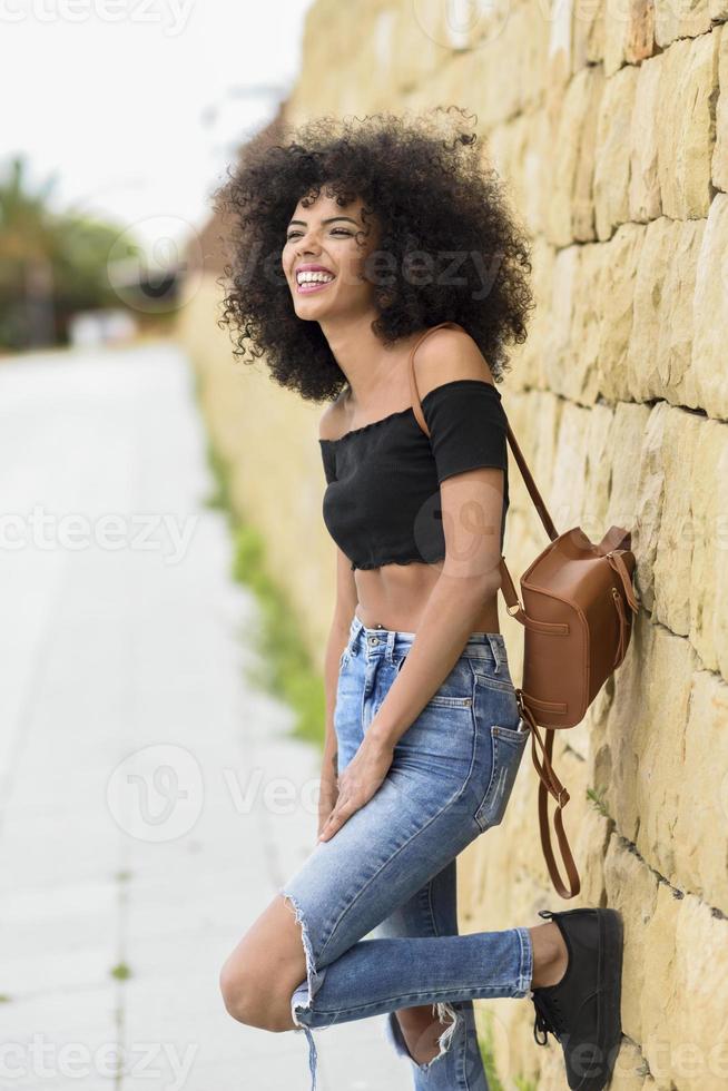 feliz mujer mixta con cabello afro riendo al aire libre foto