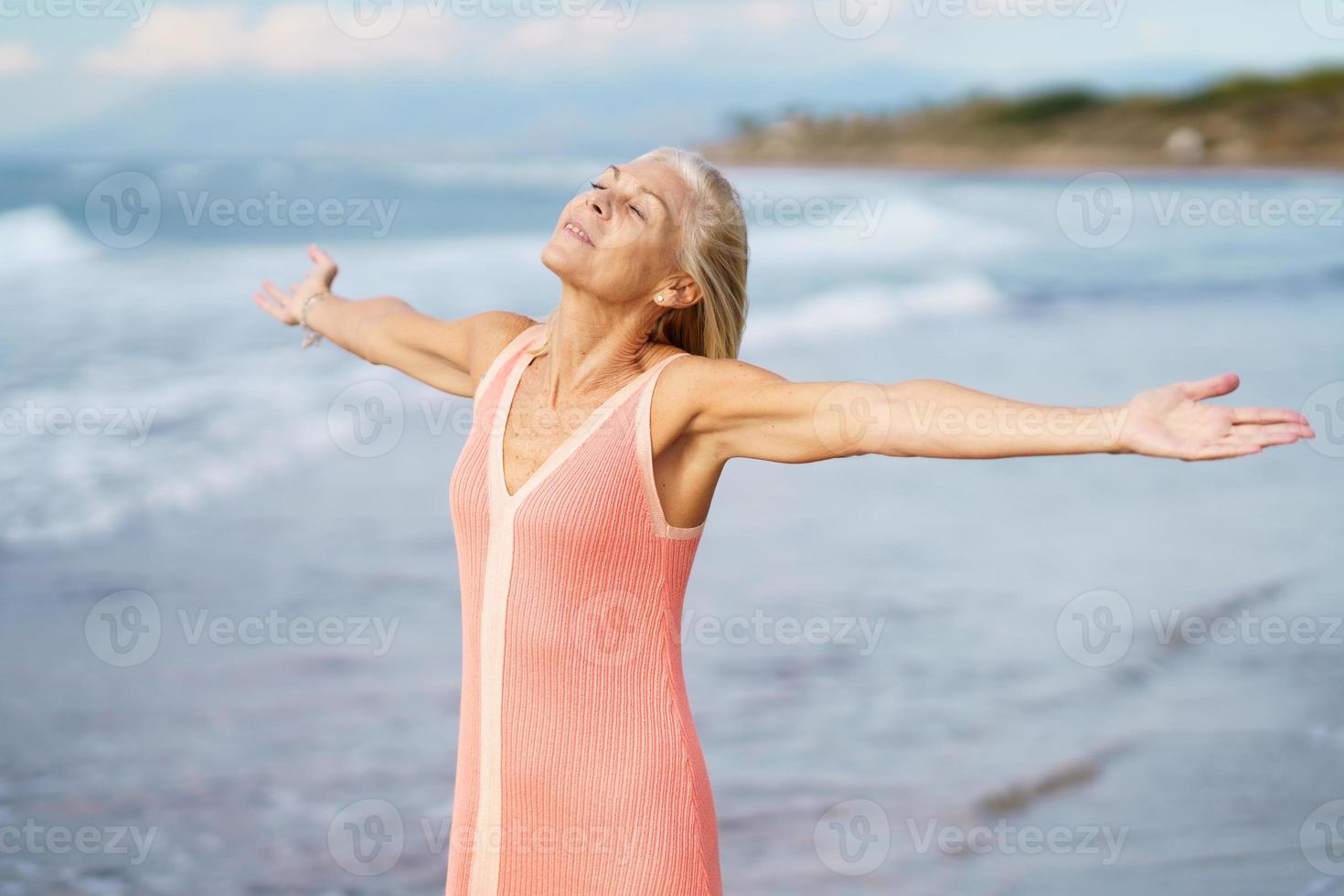 Beautiful older female spreading her arms on a beautiful beach, spending her leisure time. photo